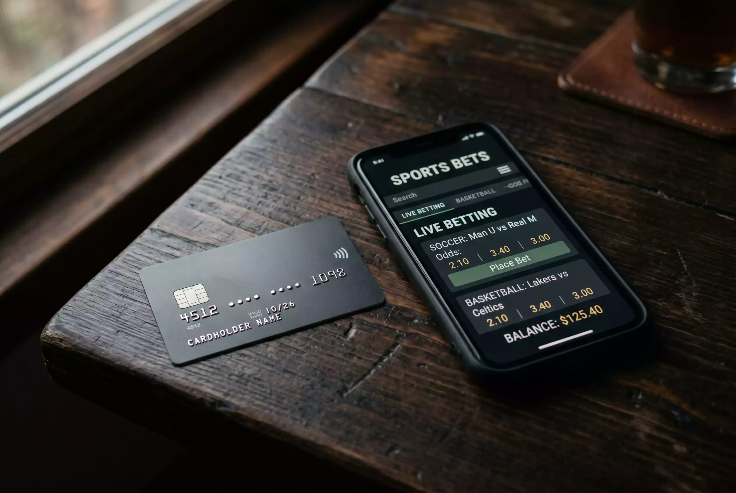 Kreditkarte und Smartphone mit einer Sportwetten-App auf einem dunklen Tisch
