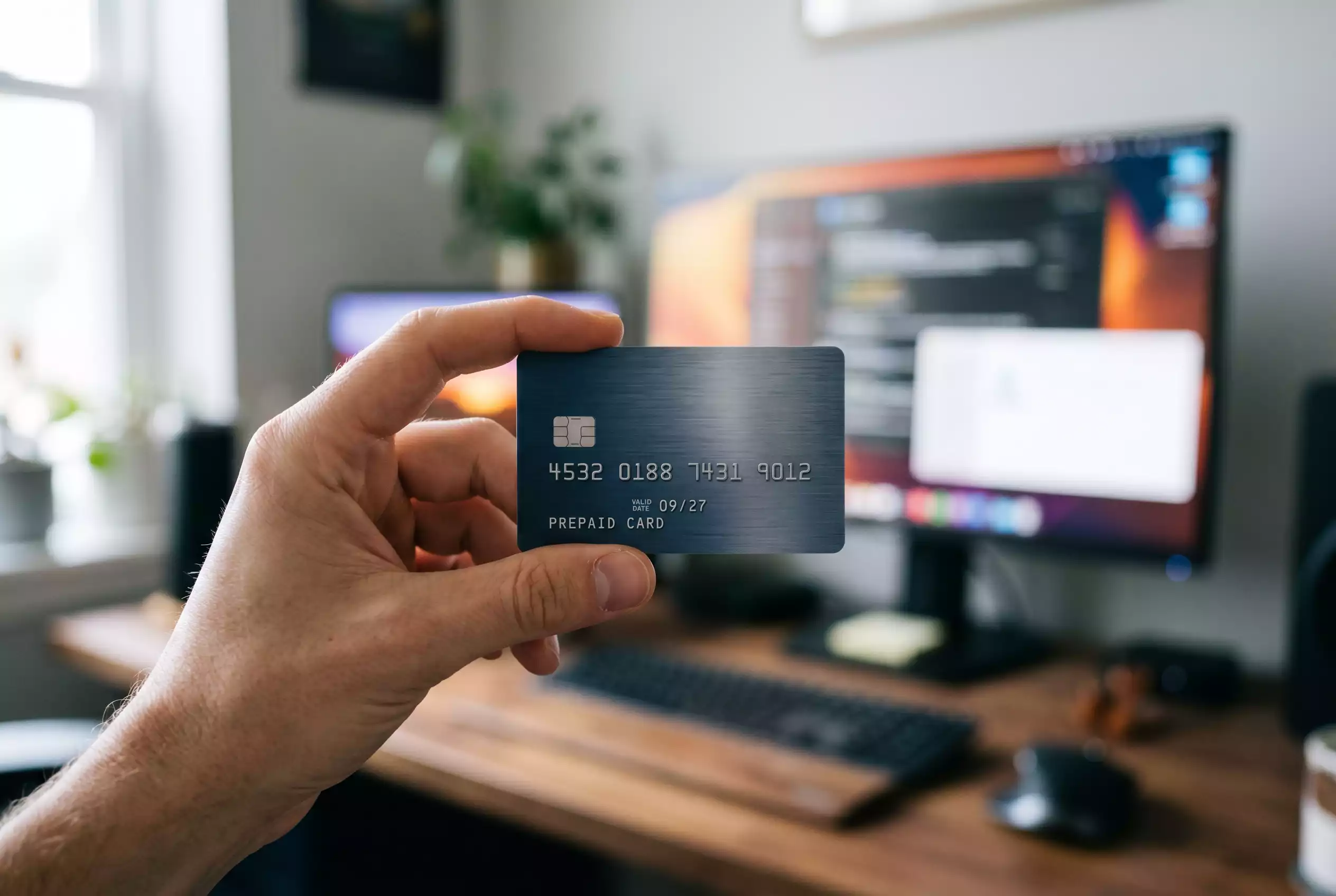 Prepaid-Kreditkarte in der Hand einer Person vor einem unscharfen Bildschirmhintergrund
